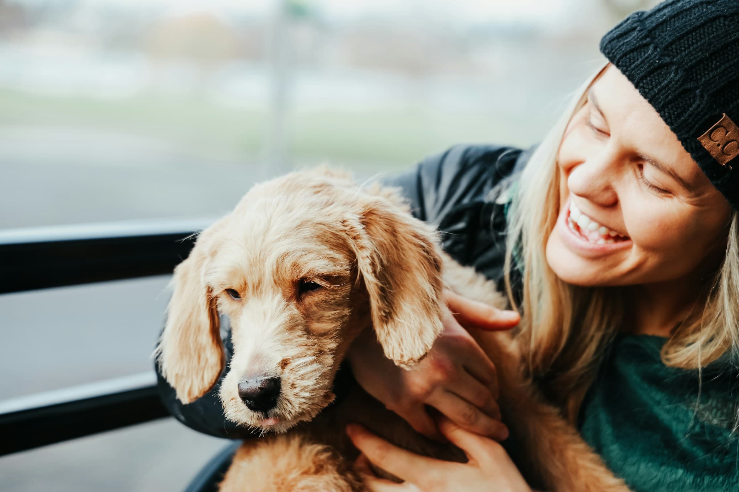 A laughing blonde woman cuddling her golden retriever puppy outdoors